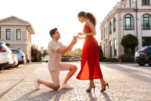 男性が指輪を持ってひざまづき、赤いドレスを着た女性にプロポーズしている