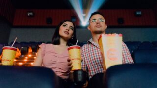 男女がポップコーンとジュースを持って映画館で鑑賞している
